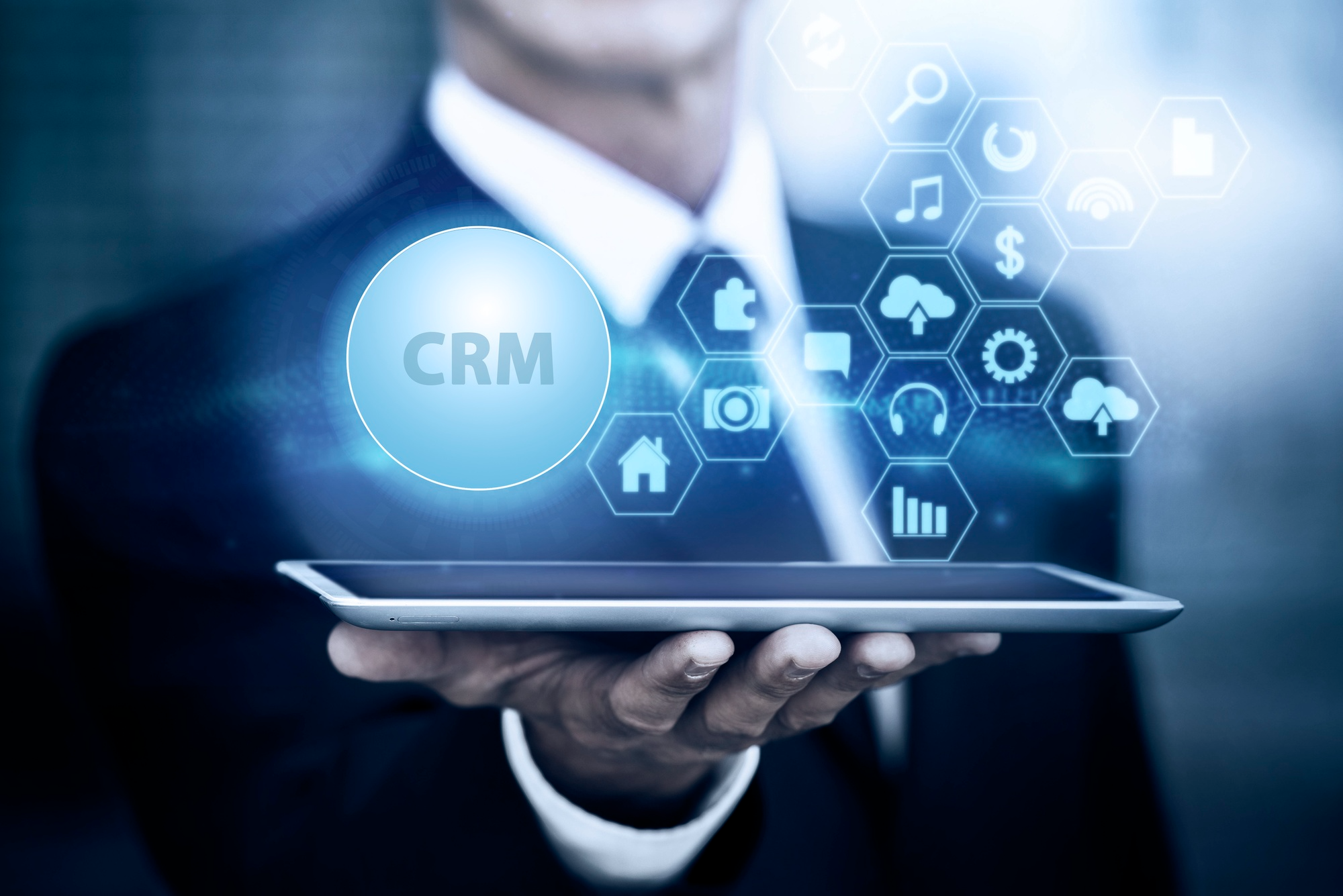 A businessman holding a tablet displaying CRM icons.
